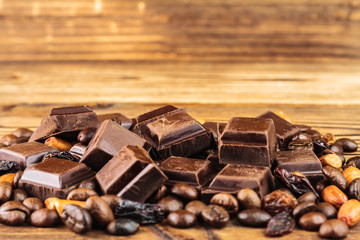 Dark chocolate cubes, coffee beans, peanuts and raisins on wooden table, close-up
