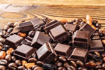 Dark chocolate cubes, coffee beans, peanuts and raisins on wooden table, close-up