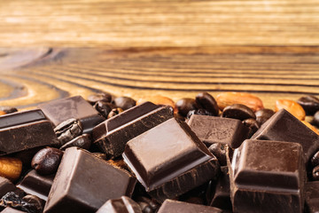 Dark chocolate cubes, coffee beans, peanuts and raisins on wooden table, close-up