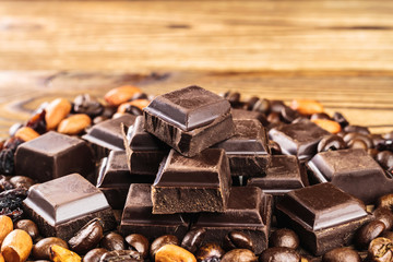 Dark chocolate cubes, coffee beans, peanuts and raisins on wooden table, close-up