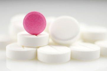 Close-up. Pharmacy theme. Pink pill standing on a heap of white pills.