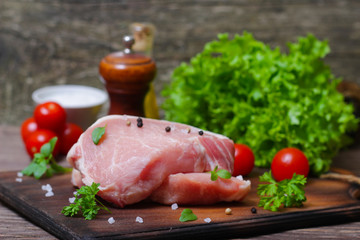 Sliced pieces of raw meat for barbecue with fresh Vegetables (tomatoes, lettuce) on wooden surface. Meat raw stacked on wooden background, beef Steak BBQ. 