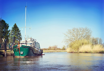 Fototapeta premium Sunny riverside with marshland and reeds. View from a boat to a river with little pier or jetty in springtime.