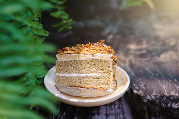 Piece of mocca almond cake on wood plate with green leaves backg