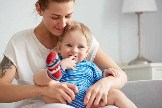 Young mother with her one years old little son are helps son to take the first steps in the bedroom at the weekend together.  Selective focus. Casual lifestyle photo series in real life interior