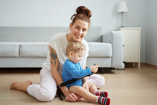 Young mother with her one years old little son dressed in pajamas are posing. Mom with son taking selfie on her smartphone or action camera in the bedroom.  Selective focus. Casual lifestyle photo.