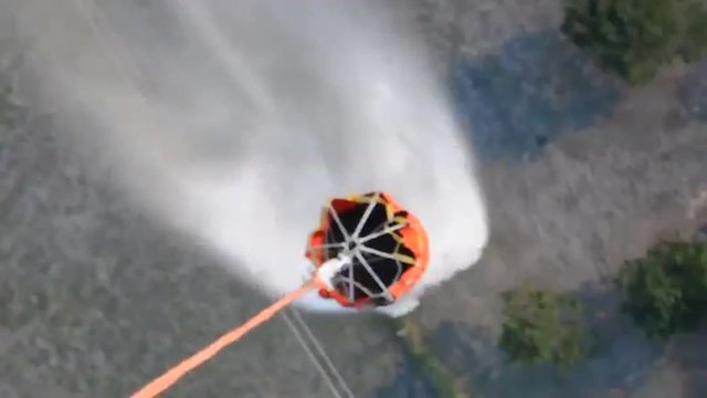 POV from a water dropping helicopter of the bucket.