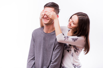 Fototapeta premium Attractive happy hipster woman with big toothy smile holding boyfriends eyes with surprise emotions. Smile girl look at happy man. Caucasian couple against white background.