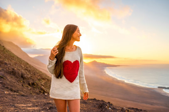 Young woman in sweater with heart shape enjoying beautiful nature on Fuerteventura island in Spain on the sunset
