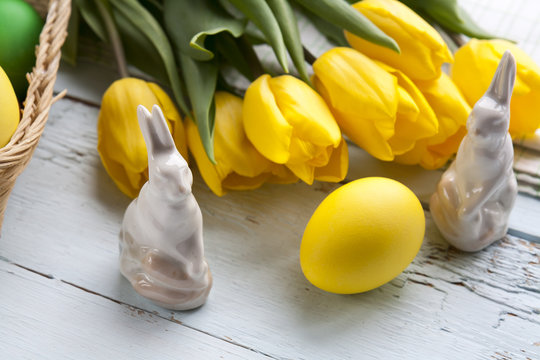 Easter decoration with yellow tulips, ceramic rabbits and colored eggs over light background