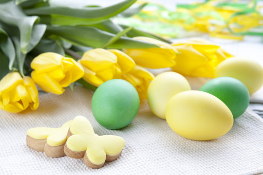 Easter eggs, homemade cookies and yellow tulips over light background with copy space