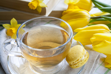 A cup of hot tea, yellow tulips, yellow daffodils, old books and lemon macaroons on a light background