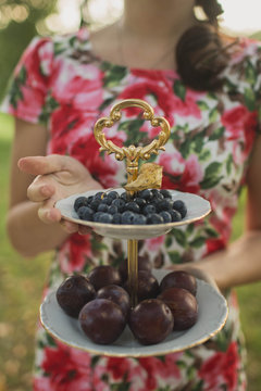 girl holding a fruit dish with plums and blueberries