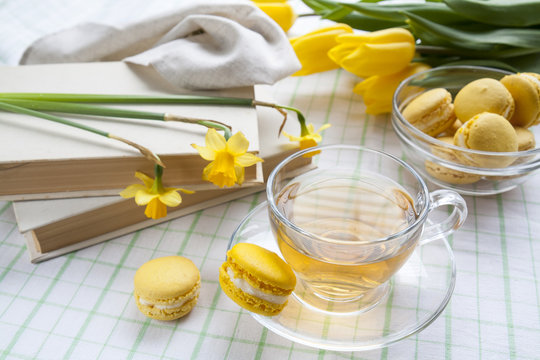 A cup of hot tea, yellow tulips, yellow daffodils, old books and lemon macaroons on a light background