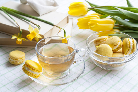 A cup of hot tea, yellow tulips, yellow daffodils, old books and lemon macaroons on a light background