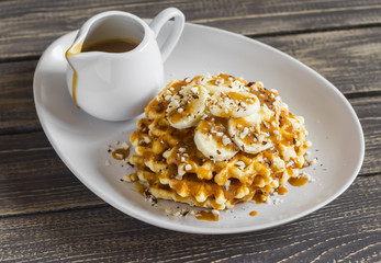 Waffles with banana slices, nuts and caramel sauce on a  wooden background
