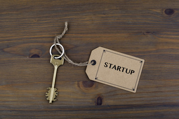 Key and a note on a wooden table with text - Startup