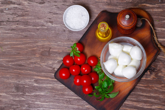 Italian cuisine. Mediterranean cuisine.  Traditional italian mozzarella cheese in glass bowl with basil, tomatoes and olive oil - caprese salad ingredients, on rustic wooden background. Rustic style