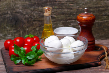 Italian cuisine. Mediterranean cuisine.  Traditional italian mozzarella cheese in glass bowl with basil, tomatoes and olive oil - caprese salad ingredients, on rustic wooden background. Rustic style