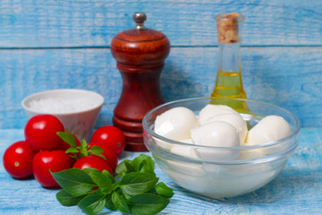 Italian cuisine. Mediterranean cuisine.  Traditional italian mozzarella cheese in glass bowl with basil, tomatoes and olive oil - caprese salad ingredients, on rustic wooden background. Rustic style
