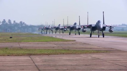 Numerous F-15 and F-16 fighter jets line up and taxi for takeoff in a military exercise.