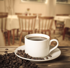 Coffee beans and coffee in white cup on wooden table opposite a