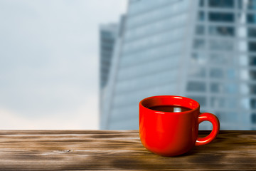 Coffee in cup on wooden table opposite a defocused cityscape for