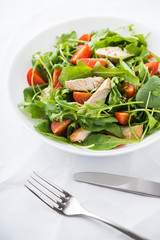 Fresh salad with chicken, tomato and greens (spinach, arugula) on white background close up. Healthy food.