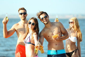 Happy young friends drinking beer at the beach, outdoors