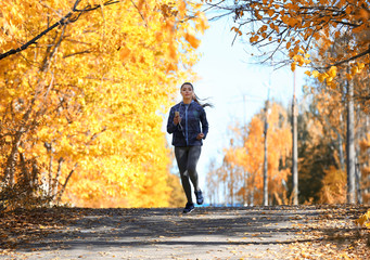 Fototapeta premium Young beautiful woman running in autumn park and listening to music with headphones.