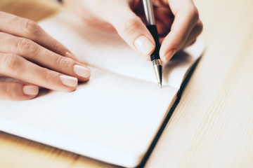 Female hands writing in notebook with pen on wooden table