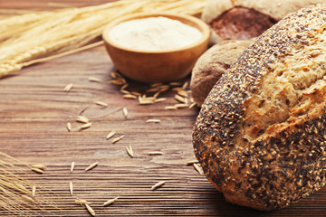 Fresh baked bread, a bowl of flour and wheat ears on the wooden background