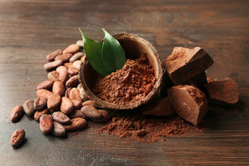 Bowl with aromatic cocoa powder and green leaf on wooden background, close up