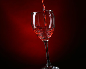 Wine pouring in glass on dark red background