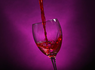 Wine pouring in glass on dark purple background