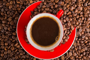 A red cup of coffee bean on the coffee beans background. Top view