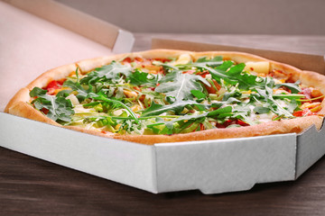 Fresh pizza in cardboard box on wooden table closeup