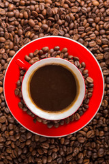 A red cup of coffee bean on the coffee beans background. Top view