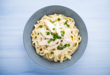Pasta fettuccine alfredo with chicken, parmesan and parsley on blue wood background top view. Italian cuisine.