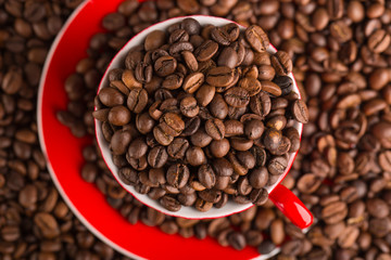 A red cup of coffee bean on the coffee beans background. Top view