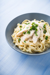 Pasta fettuccine alfredo with chicken, parmesan and parsley on blue wood background close up. Italian cuisine.