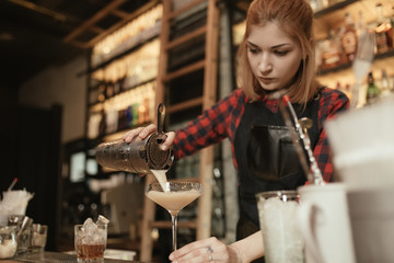 Woman bartender pouring alcohol cocktail in wineglass from shaker