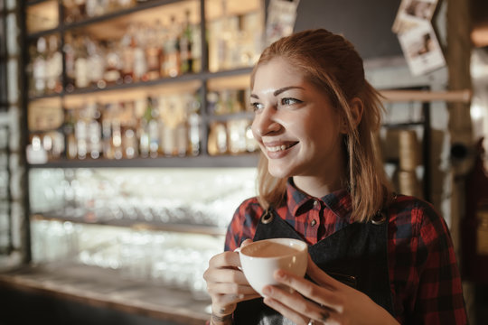 Break in work. Smiling woman barista drinks coffee.