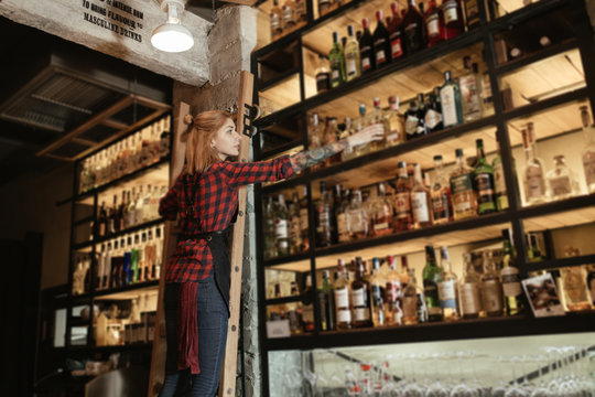 Bartender selecting a bottle of wine on bar shelves
