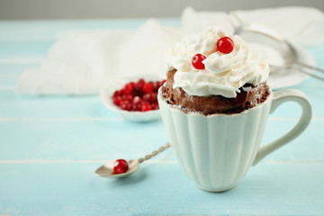 Mug cake with cream and cranberry on blue wooden background