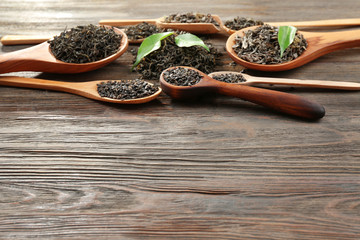 Dry tea with green leaves in wooden spoons on table background, copy space