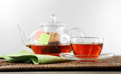 Cup of tea with tea bags and teapot on wooden background against grey background