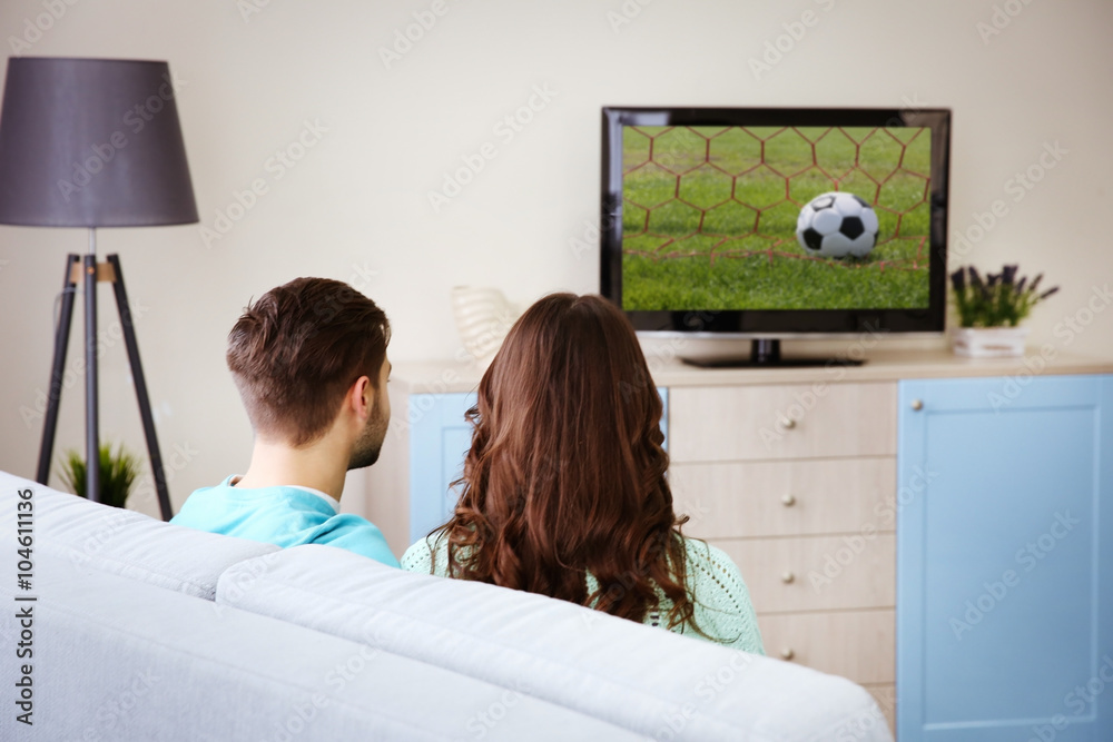 Wall mural young couple watching tv on a sofa at home