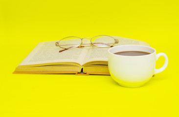 Cup of coffee with book isolated on yellow background