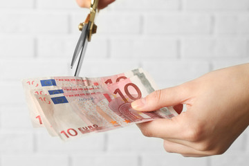 Hands with scissors cutting money on white brick wall background